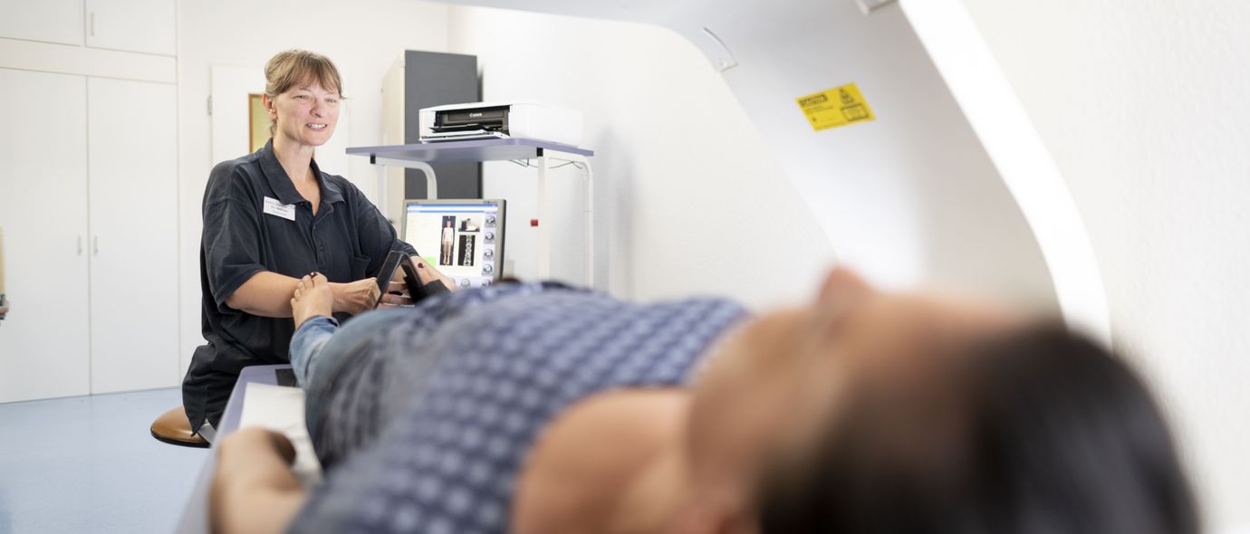 Pflegekraft bereitet liegenden Patienten zur Knochendichtemessung vor