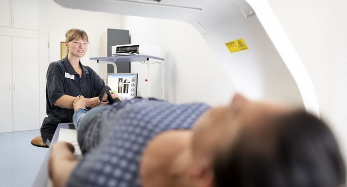 Pflegekraft bereitet liegenden Patienten zur Knochendichtemessung vor