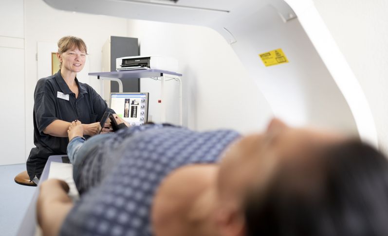 Pflegekraft bereitet liegenden Patienten zur Knochendichtemessung vor